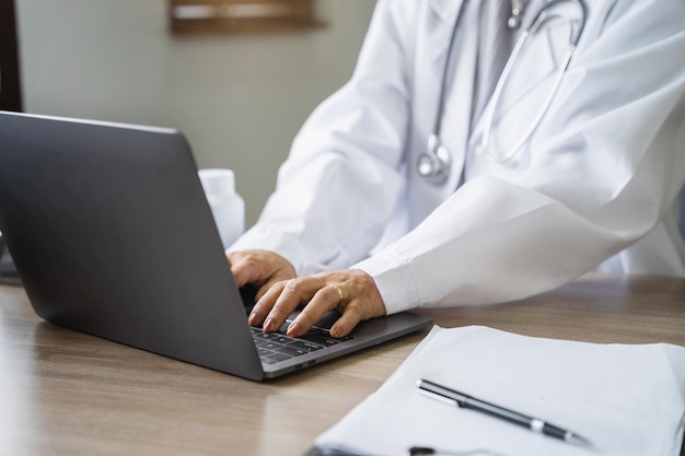 Doctor working with laptop computer and writing on paperwork in the room