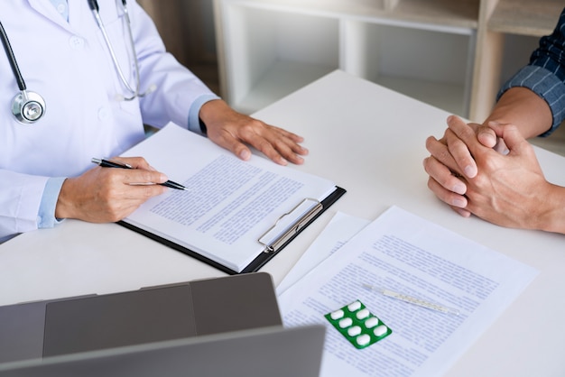 Doctor working with patient taking notes with clipboard and discussing something in his medical office, health care and people concept.