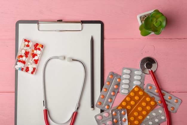 空白のクリップボードの薬の赤い聴診器と丸薬のある医師の職場薬の処方箋