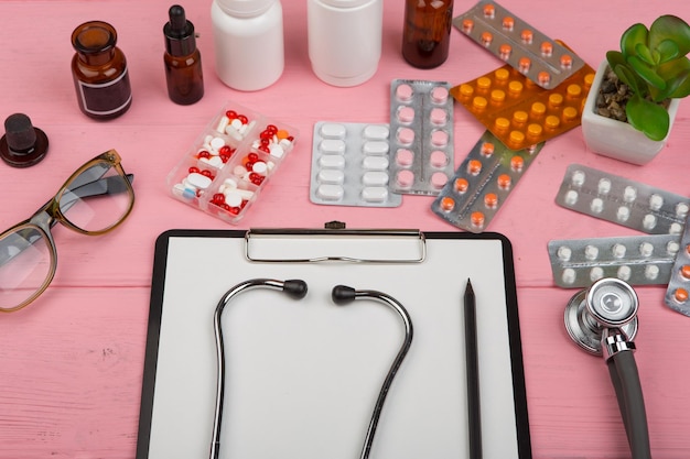 Doctor workplace with blank clipboard red stethoscope on pink wooden table Medication prescription