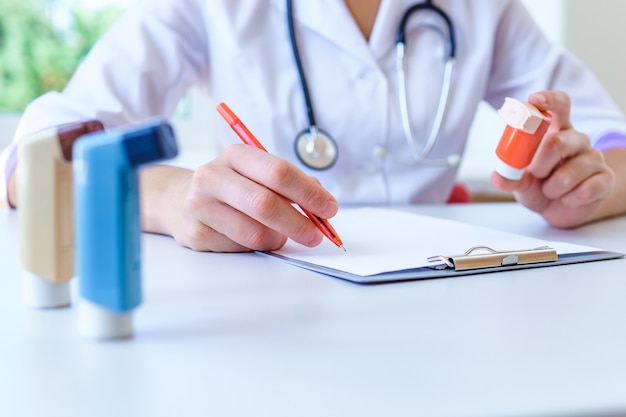 Doctor writes medical prescription for asthma inhaler to asthmatic patient during medical consultation and examination in hospital. Healthcare