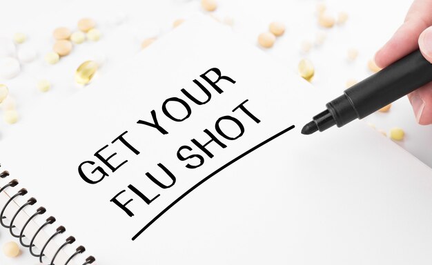 사진 의사가 흰색 메모장에 get your flu shot이라는 단어를 씁니다.