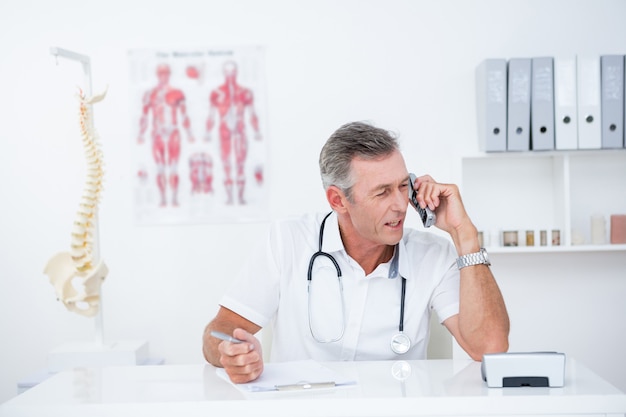 Doctor writing on clipboard and phoning