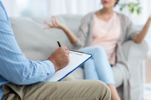 Doctor writing on clipboard while consulting pregnant woman at home