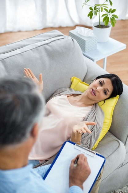 Doctor writing on clipboard while consulting pregnant woman at home