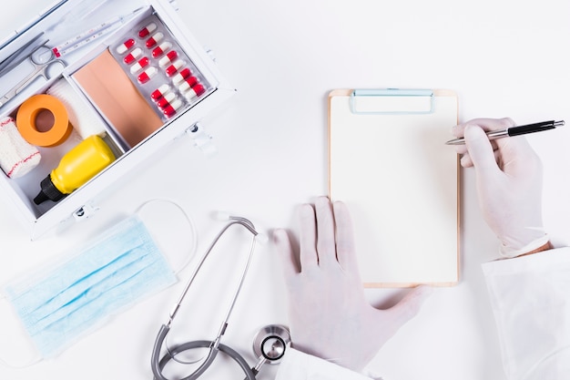 Photo doctor writing on clipboard with medical equipments on white backdrop