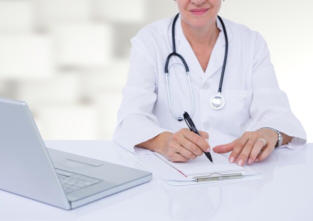 Doctor writing at desk against white blurry pattern