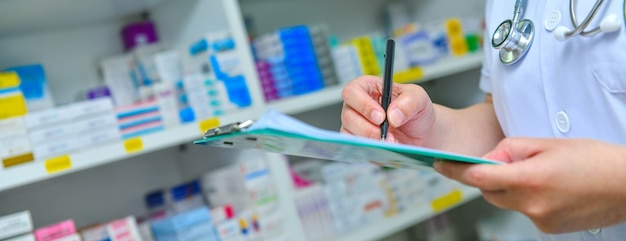 Doctor writing prescription with many medicine on shelvesbackground