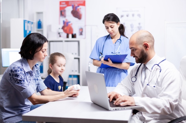 doctor writing treatment on laptop during consultation of child and mother in hospital office. healthcare physician specialist in medicine providing health care services treatment examination.
