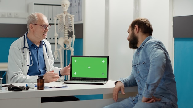 Doctor and young patient using laptop with greenscreen on office desk at checkup appointment. Analyzing isolated chroma key template with blank mockup and copyspace background.