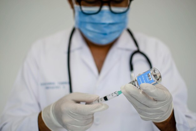 Doctors are experimenting with vaccination against the coronavirus Scientists are using a syringe A man wearing a mask holds a syringe and a vaccine bottle Concept of the laboratory vaccine trial