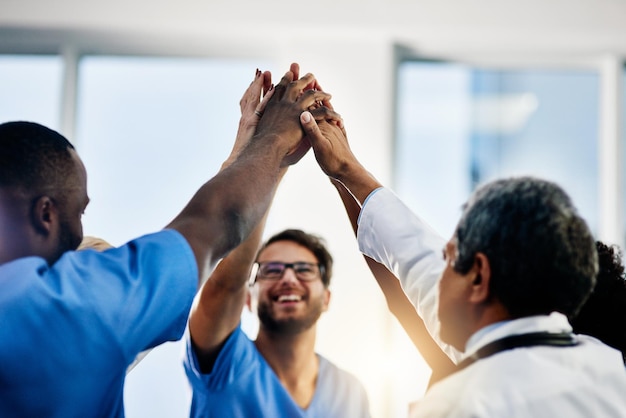 Photo doctors celebrating medical success after working together as a team and give each other motivating a high five as a group in a hospital healthcare workers joining hands in a huddle showing teamwork