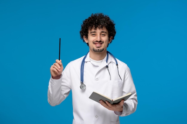 Doctors day curly brunette cute guy in lab coat smiling with pen and book