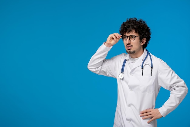 Doctors day curly brunette cute guy in medical uniform looking far very confusingly