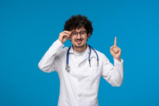 Doctors day curly brunette cute guy in medical uniform wearing glasses and smiling