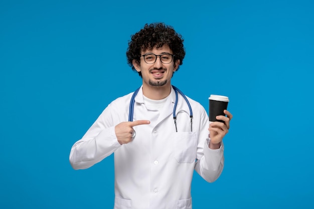 Doctors day curly handsome cute guy in medical uniform pointing at paper cup