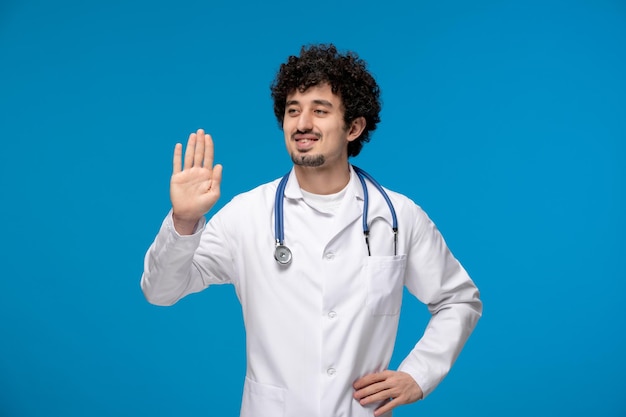 Doctors day curly handsome cute guy in medical uniform showing stop hand gesture