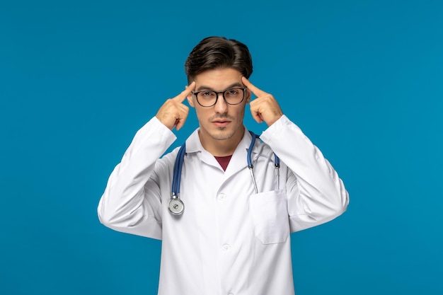 Doctors day cute young brunette guy in lab coat wearing glasses thinking and touching temples