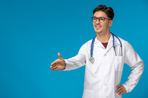 Doctors day cute young handsome man in lab coat and glasses giving hand for a handshake