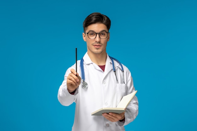 Doctors day cute young handsome man in lab coat and glasses holding pen and notebook