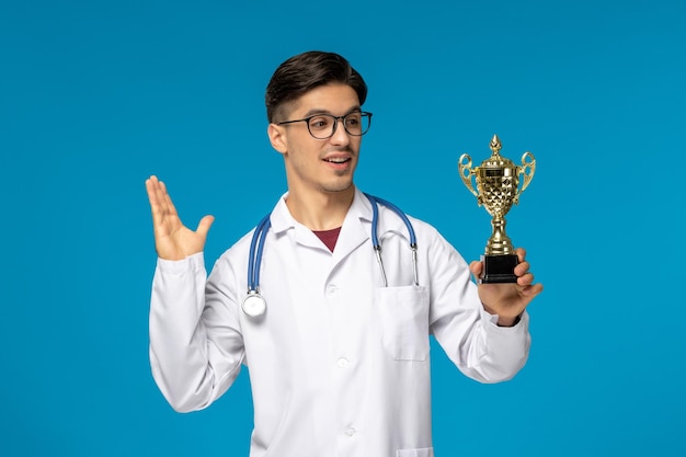 Doctors day cute young handsome man in lab coat and glasses looking at golden trophy