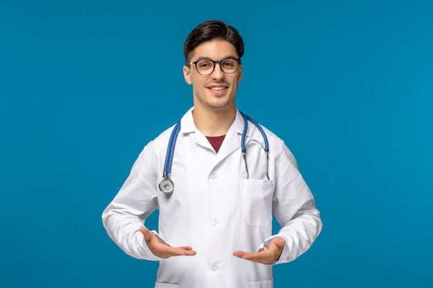 Doctors day handsome brunette cute guy in medical gown smiling with open hands