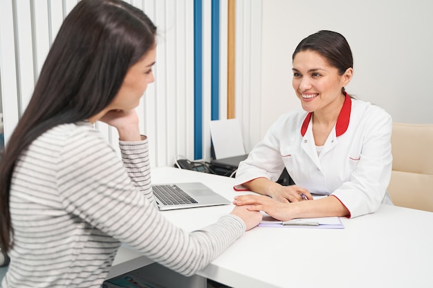 Doctors examination. Cheerful young practitioner keeping smile on her face while consulting her visitor