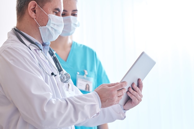 Doctors in facial masks viewing online data on digital tablet while discussing coronavirus test results