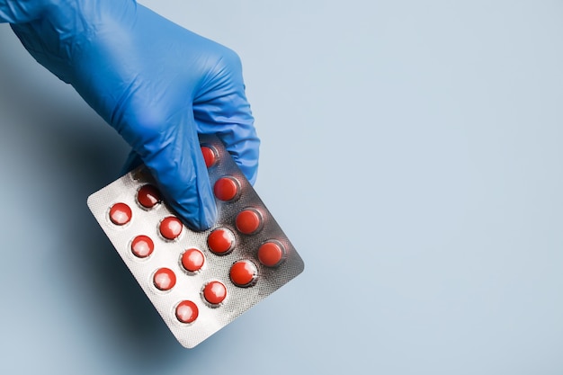 The doctors hand in a blue protective glove holds out pills in a blister