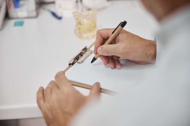 doctors hand holding a pen and making notes on a blank paper