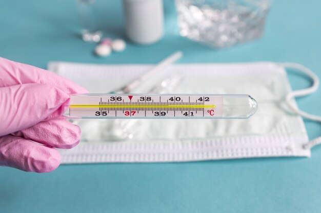 Doctors hand in pink latex glove holding thermometer indicating high temperature. Healthcare and medicine concept.
