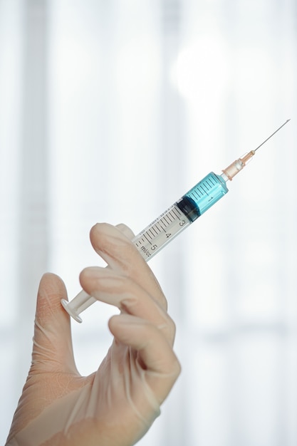 Doctors hand in rubber glove holding syringe with vaccine or medicine