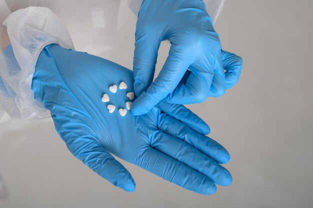 The doctors hands in rubber gloves hold heartshaped pills