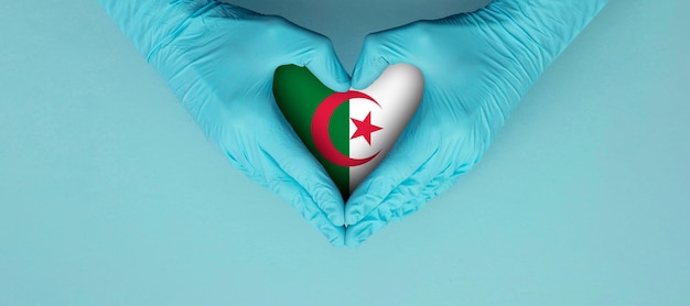 Doctors hands wearing blue surgical gloves making hear shape symbol with algeria flag