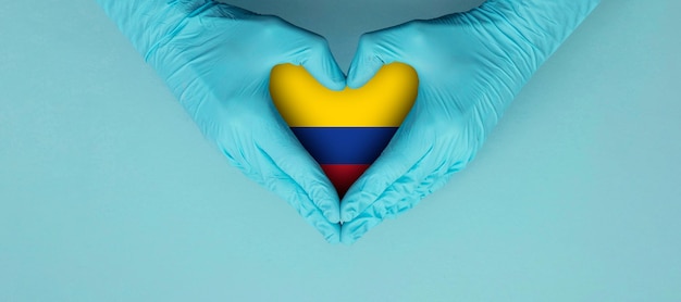 Mani dei medici che indossano guanti chirurgici blu che fanno sentire il simbolo della forma con la bandiera della colombia