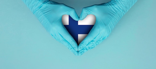 Doctors hands wearing blue surgical gloves making hear shape symbol with finland flag