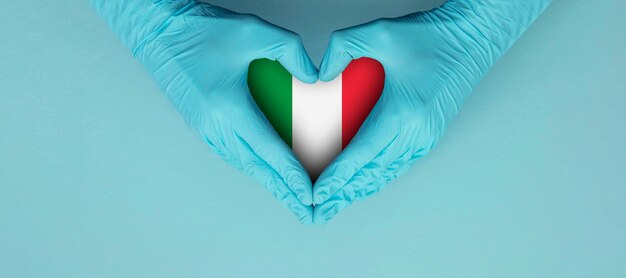 Photo doctors hands wearing blue surgical gloves making hear shape symbol with italy flag