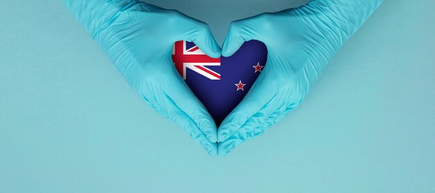 Doctors hands wearing blue surgical gloves making hear shape symbol with new zealand flag