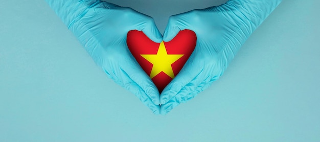 Doctors hands wearing blue surgical gloves making hear shape symbol with vietnam flag