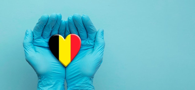 Руки врачей в хирургических перчатках держат сердце флага бельгии