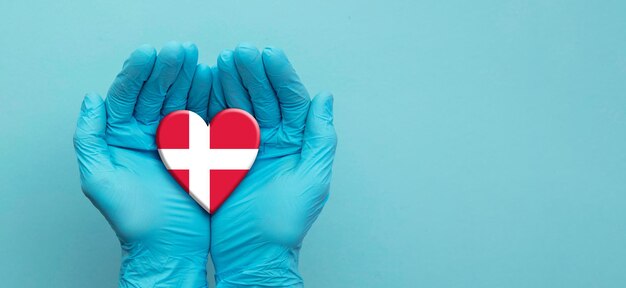 デンマークの旗の心臓を保持している手術用手袋を着用して医師の手