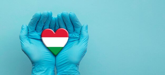 Doctors hands wearing surgical gloves holding hungary flag heart