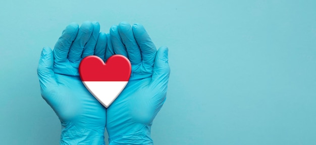 Photo doctors hands wearing surgical gloves holding indonesia flag heart