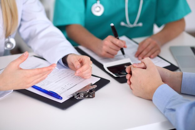 Doctors and patient are discussing something, just hands at the table.