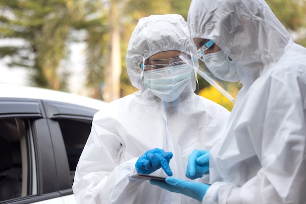 Doctors in ppe suit using tablet with face shield discussing standing on street