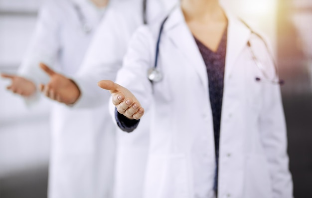 Doctors standing as a team while offering helping hand for shaking hand or saving life in sunny clinic. Medicine concept.