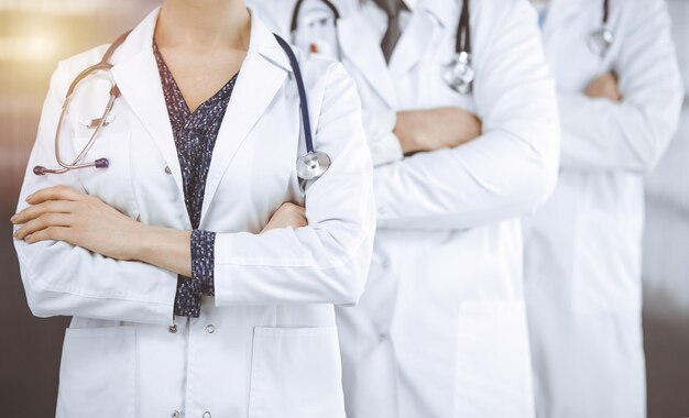 Doctors standing as a team with arms crossed in sunny clinic. Medical help, insurance and medicine concept.