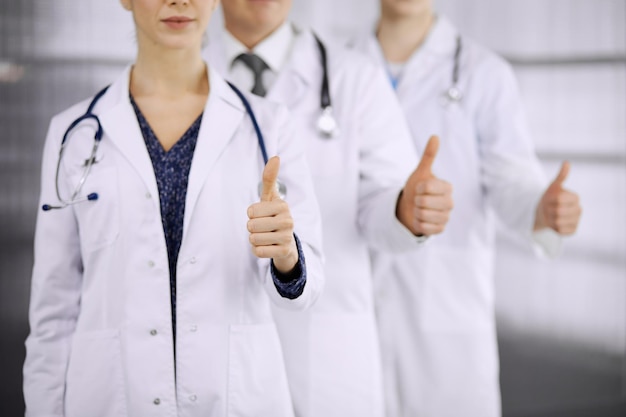 医師はクリニックで親指を立ててチームとして立ち、患者を助ける準備ができています。医療支援、保険、薬のコンセプト。