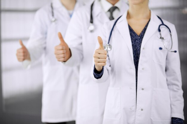 Doctors standing as a team with thumbs up in clinic and ready to help patients. Medical help, insurance and medicine concept.