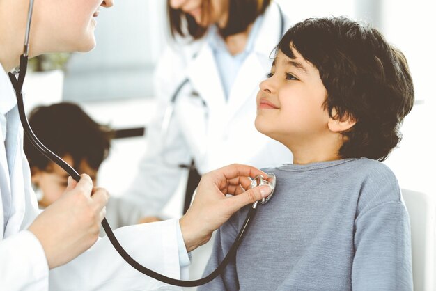 Doctorwoman examining a child patient by stethoscope cute arab\
boy at physician appointment medicine concept